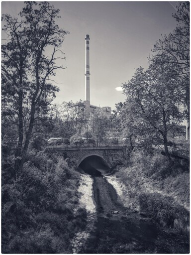 It's a monochrome photo of a factory and at the bottom you see a creek and it looks like basically the output from the factory is going through the creek. 