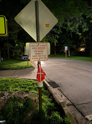picture of an intersection with a sign warning pedestrians to wave a red flag when crossing, for their safety.